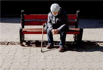 Eine ältere Frau mit Mund-Nasen-Schutz sitzt auf der Bank.