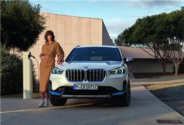 Eine Frau im Business-Kostüm lehnt an einem BMW X1, der gerade elektrisch geladen wird.