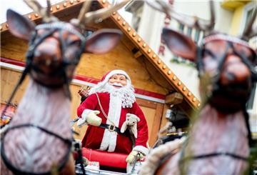 Ein Weihnachtsmann auf einem Schlitten und zwei Rentiere stehen als Dekoration an einem Marktstand auf einem Weihnachtsmarkt.