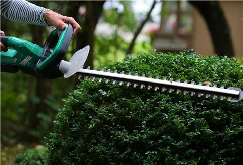 Eine Person schneidet eine Hecke. 