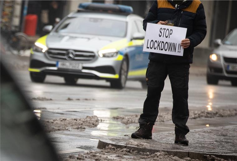 Ein Mann hält ein Schild mit der Aufschrift "Stop Lockdown!!" während einer spontanen Demonstration nach einer Durchsuchung bei einem Arzt.