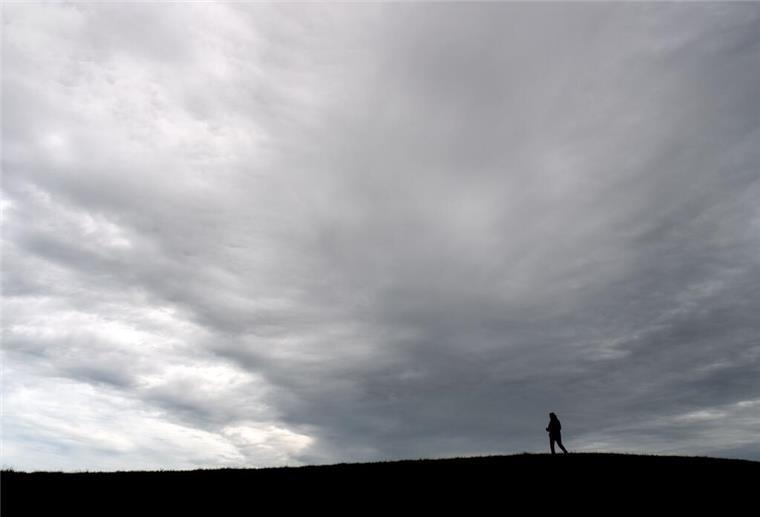 Schauer und Gewitter in Niedersachsen und Bremen erwartet Dunkle Wolken ziehen vorüber, während ein Spaziergänger über einen Deich geht.