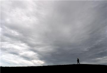 Dunkle Wolken ziehen vorüber, während ein Spaziergänger über einen Deich geht.