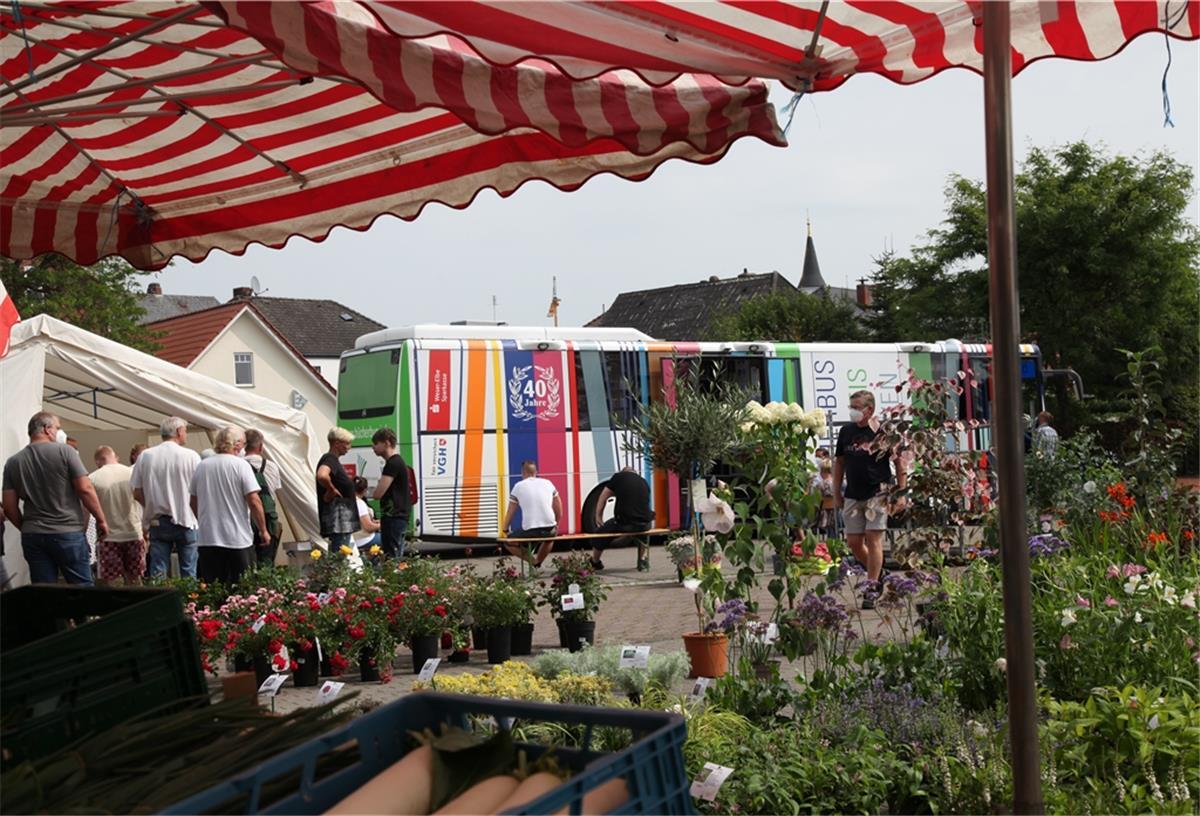 Der Impfbus des Landkreises (umgenutzter Bücherbus) steht am Freitag auf dem Wochenmarkt in Beverstedt. Im Vordergrund sind Blumen zu sehen. 