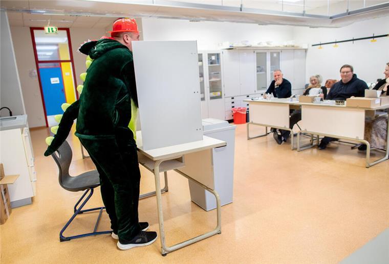 Der kostümierte Wähler Christopher steht in einem Wahllokal bei der Stimmabgabe hinter einem Sichtschutz.