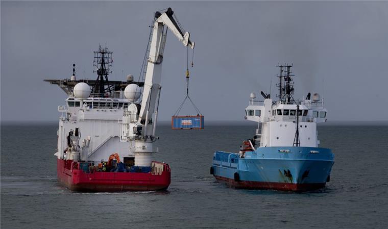 Der Kran des Offshore-Versorgungsschiffs hebt einen Container auf ein anderes Schiff. Von dort wird er zu einem nahe gelegenen Hafen transportiert. Ab Donnerstag soll auch auf deutscher Seite mit der Bergung begonnen werden. 