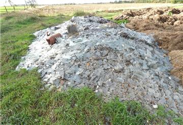 Neben einem Misthaufen auf einem Feld liegt ein Haufen mit Abfall aus Schutt und Scherben.