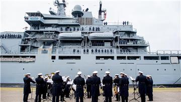 Der Marinemusikkorps Wilhelmshaven steht an einer Kaimauer, während die „Frankfurt am Main“ in den Hafen einfährt.