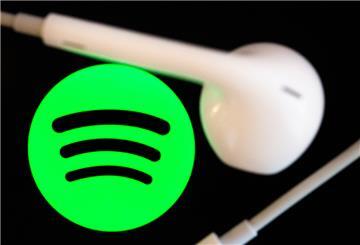 Kopfhörer liegen auf dem Bildschirm eines Smartphones, auf dem das Logo vom Musikstreaming-Dienst Spotify angezeigt wird.