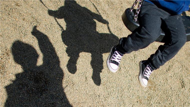 Der Schatten von einem Mann und einem schaukelnden Kind auf einem Spielplatz.