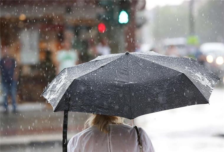  Ein Frau steht bei einem kurzen Regenschauer mit einem Regenschirm an einer Ampel