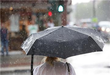  Ein Frau steht bei einem kurzen Regenschauer mit einem Regenschirm an einer Ampel