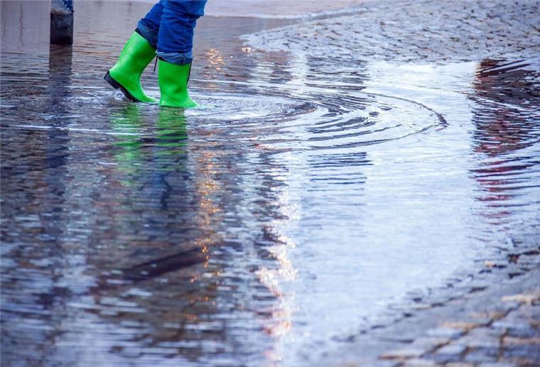 ARCHIV - Mit Gummistiefeln geht eine Frau über eine leicht überflutete Straße. Foto: Jens Büttner/dpa-Zentralbild/dpa/Symbolbild