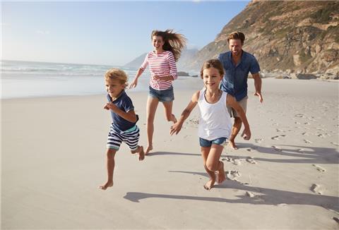 Eine Familie läuft lächelnd in sommerlicher Kleidung über einen Sandstrand.