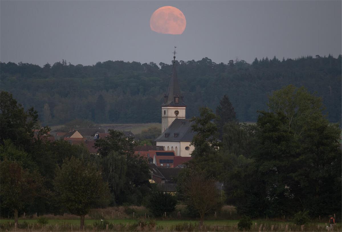 Der Supermond geht hinter der Kirche von Wehrheim im hessischen Taunus auf.