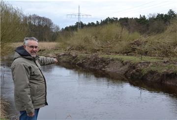 Der Vorsitzende des Angelsportvereins, Dirk Glaß, steht am Ufer der Oste und zeigt auf die gefällten Bäume