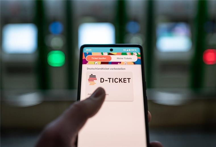 Ein Mann hält ein Mobiltelefon, auf dem das „D-Ticket“ gekauft werden kann, vor Ticketautomaten am Hauptbahnhof in der Hand