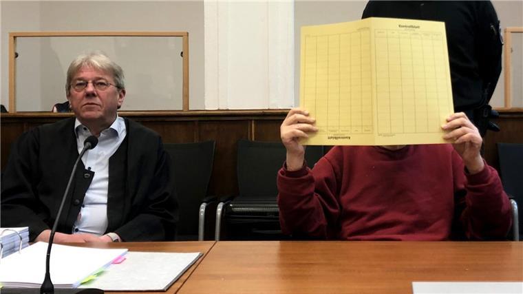 Mutter mit Kissen erstickt: Sohn zu Haftstrafe verurteilt Der wegen Mordes vor dem Landgericht Angeklagte hält sich eine gelbe Pappmappe vor das Gesicht.