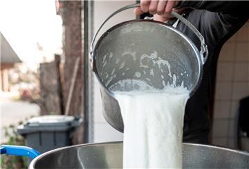 Ein Landwirt kippt Milch aus einem Eimer in ein Abholgefäß
