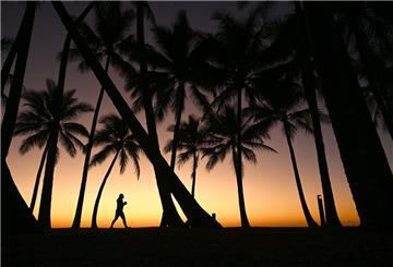 Eine Person geht am Strand entlang, während die Sonne über Palm Cove, nördlich von Cairns in Queensland, aufgeht.