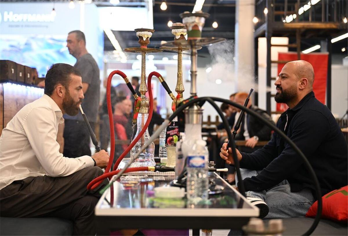 Besucher der Fachmesse Intertabac sitzen an einem Tisch und inhalieren Dampf aus Wasserpfeifen (Shishas).