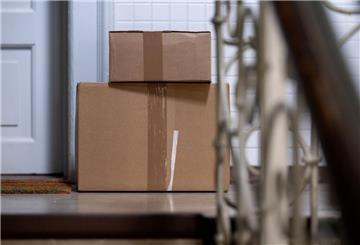 Zwei Pakete liegen in einem Mehrfamilienhaus im Treppenhaus vor einer Wohungstür.