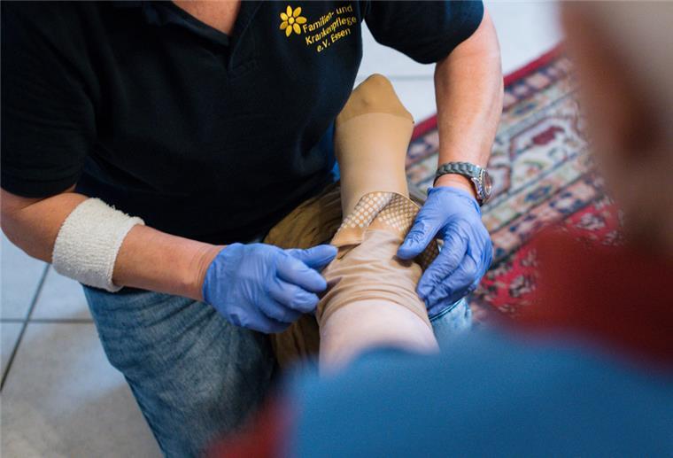 Eine ambulante Pflegerin hilft einer alten Frau einen Stützstrumpf anzuziehen