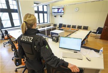 Eine Justizbeamtin steht in einem Gerichtssaal, in dem eine Zeugenvernehmung mittels Video aus einem Nebenraum übertragen werden kann.