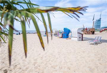 Strandkörbe und eine Sonnenliege stehen im Weserstrandbad in Bremerhaven auf hellem Sand. Im Hintergrund ist das Sail-City-Hotel zu sehen.