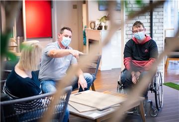 Die Bauherren Yvonne und Marvin Holst schauen mit Raumausstatter Christian Schnakenberg verschiedene Design-Bodenbeläge in Holzoptik an.