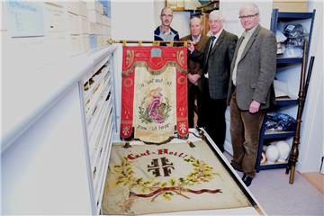 Die beiden Fahnen haben (von links) Rainer Meyer und Meinert Cornelius an Hans-Rudolf Mengers überreicht. Timothy Saunders bewahrt sie im Textilschrank des Nordenhamer Museums auf. Oben ist die Fahne des ehemaligen Gesangvereins Stollhamm zu sehen, unten die des TV Stollhamm.