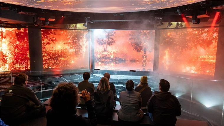 Eröffnung von Wetterextreme-Schau verzögert sich weiter Die Besucherinnen und Besucher des neuen Ausstellungsbereichs sitzen auf einer beweglichen Hubplattform. (Archivbild)