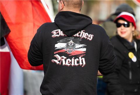 Ein Mann trägt einen Pullover mit dem Aufdruck „"Deutsches Reich" bei einer Demonstration von Reichsbürgern