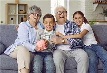 Rentner sitzen mit ihren Enkeln auf dem Sofa und halten ein Sparschwein. Die Bundesregierung plant eine Renten-Reform. Die Frühstart-Rente soll schon 2026 an den Start gehen.