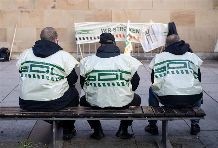 Teilnehmer eines Warnstreiks der Gewerkschaft Deutscher Lokomotivführer (GDL) sitzen vor dem Hauptbahnhof auf einer Bank.