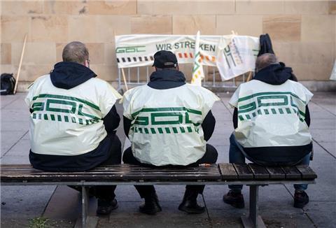 Teilnehmer eines Warnstreiks der Gewerkschaft Deutscher Lokomotivführer (GDL) sitzen vor dem Hauptbahnhof auf einer Bank.