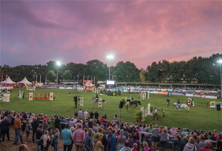 Elmloher Reitertage: Vier Tage spannender Reitsport Eine große Zuschauermenge beobachtet ein Reitturnier in abendlicher Stimmung bei Flutlicht in Wolken in Rottönen