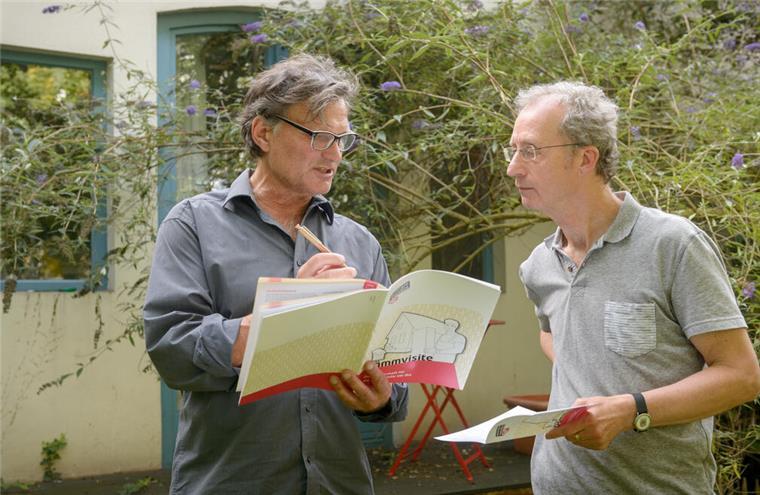 Gefragter denn je: die Dämmvisite Zwei Männer stehen vor einem Haus. der eine (der Berater) trägt Dinge in eine Mappe mit der Beschriftung "Dämmvisite" ein, der andere schaut aufmerksam zu.