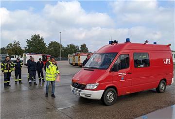 Feuerwehrleute stehen an einem roten Fahrzeug der Feuerwehr.
