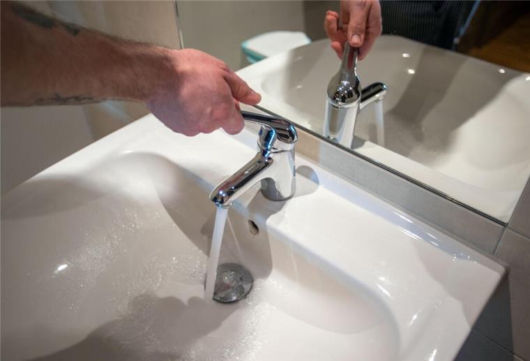Ein Mann öffnet einen Wasserhahn und lässt frisches Wasser fließen. 