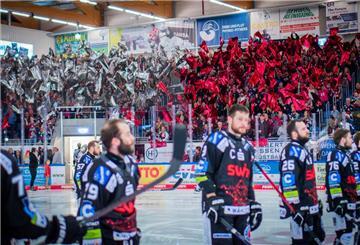 Eishockeyspieler stehen auf dem Eis. Die Fans auf der Tribüne halten rote und weiße Fahnen hoch.