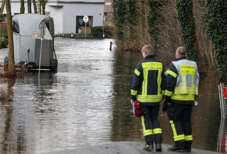 Feuerwehrleute stehen an einer überfluteten Wohnstraße