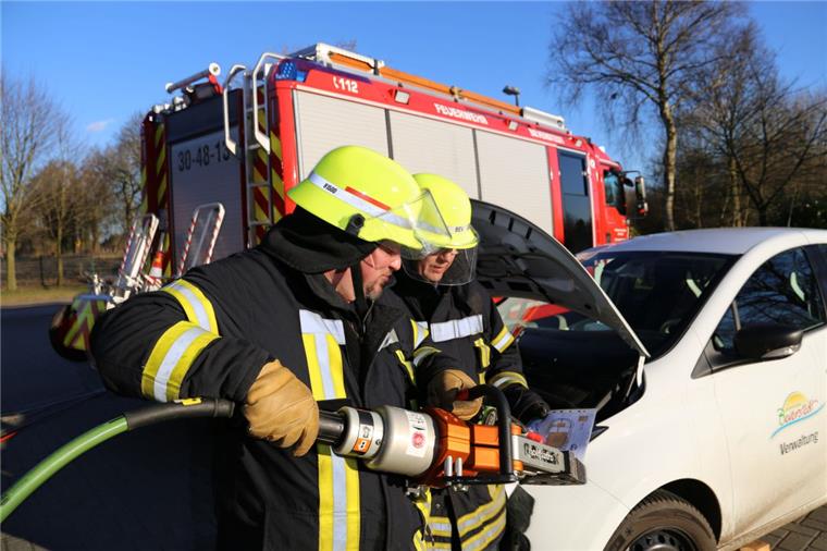 Die Feuerwehrleute Carsten Salinski (links) und Axel Brünjes beim Einsatz am Elektro-Auto. Während Salinski schon die Rettungsschere bereithält, studiert Brünjes das Rettungsdatenblatt des Flitzers. Dort ist vermerkt, wo die gefährlichen Hochvolt-Leitungen verlaufen. Fotos (2) Gehrke