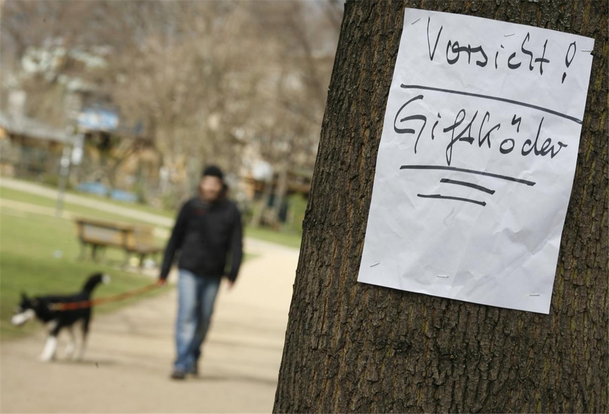 Giftköder: Tasso gibt Tipps für den Notfall Zettel am Baum: Vorsicht Giftköder. Im Hintergrund Mann mit Hund.