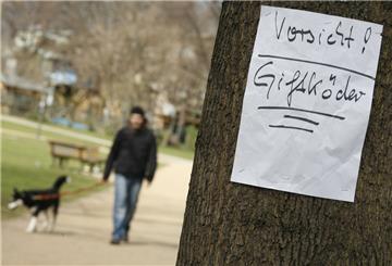 Zettel am Baum: Vorsicht Giftköder. Im Hintergrund Mann mit Hund.