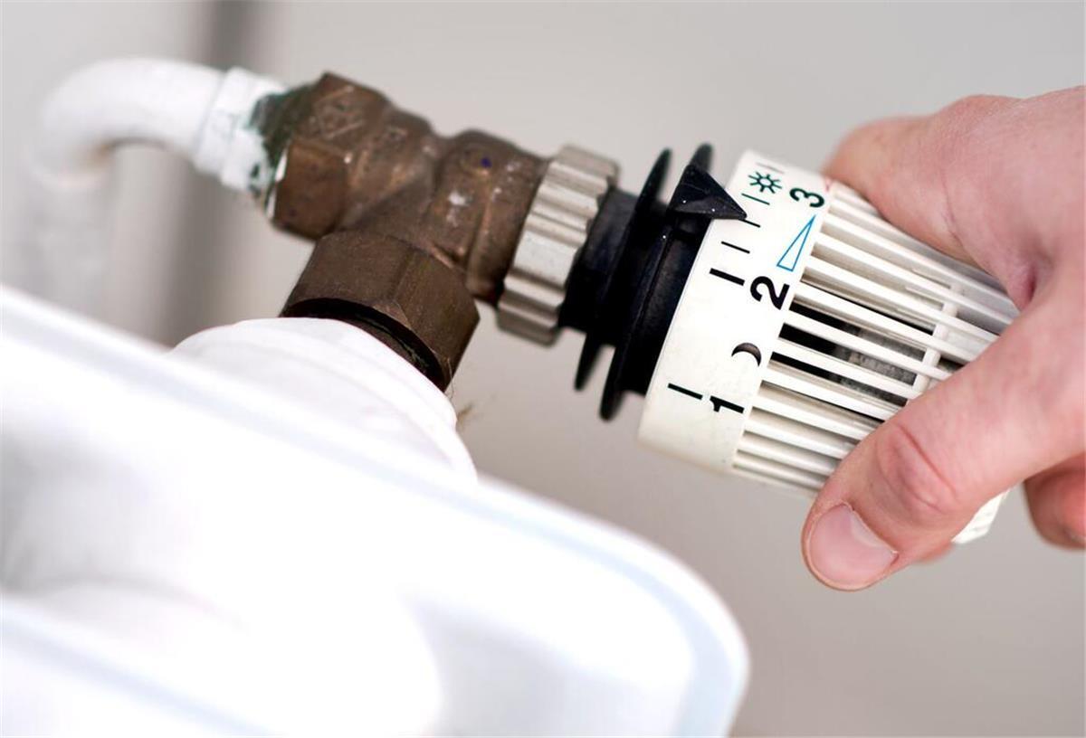 Eine Frau dreht am Thermostat eines Heizkörpers.