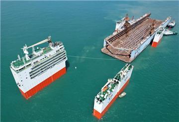 Das halbtauchfähige Schwerlastschiff „Hua Rui Long“ bei geöffneter Deckstruktur auf See, bereit zur Aufnahme eines großen Objekts; mehrere Schlepper unterstützen das Manöver.