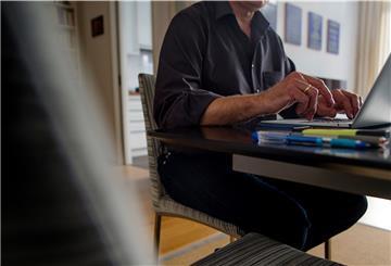 Ein Mann sitzt zuhause an einem Esstisch und arbeitet an einem Laptop. (Gestellte Szene)