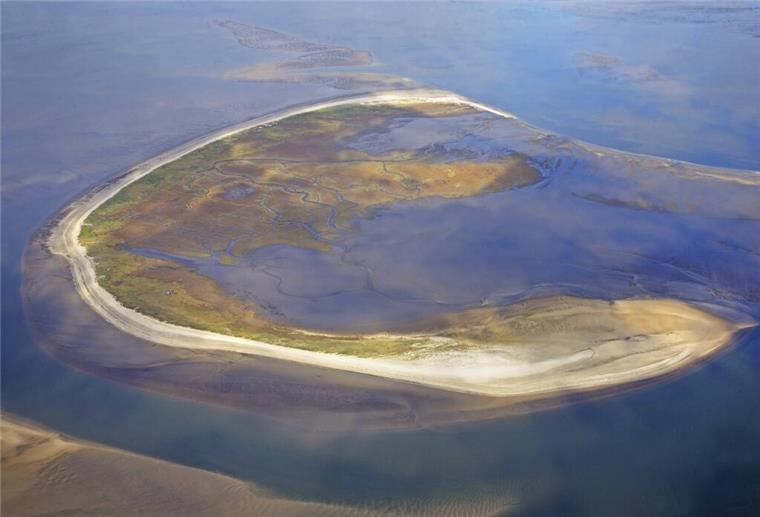 Luftfoto einer Insel. Die Insel Trischen wandert jährlich rund 30 Meter ostwärts durch das Wattenmeer. Ihre ständige Veränderung zeigt, wie dynamisch die Natur an der Nordseeküste wirklich ist.