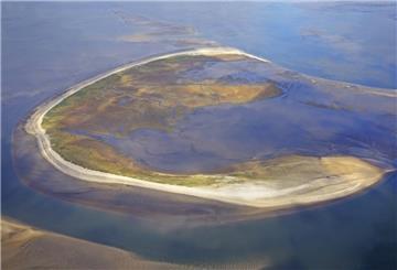 Luftfoto einer Insel. Die Insel Trischen wandert jährlich rund 30 Meter ostwärts durch das Wattenmeer. Ihre ständige Veränderung zeigt, wie dynamisch die Natur an der Nordseeküste wirklich ist.